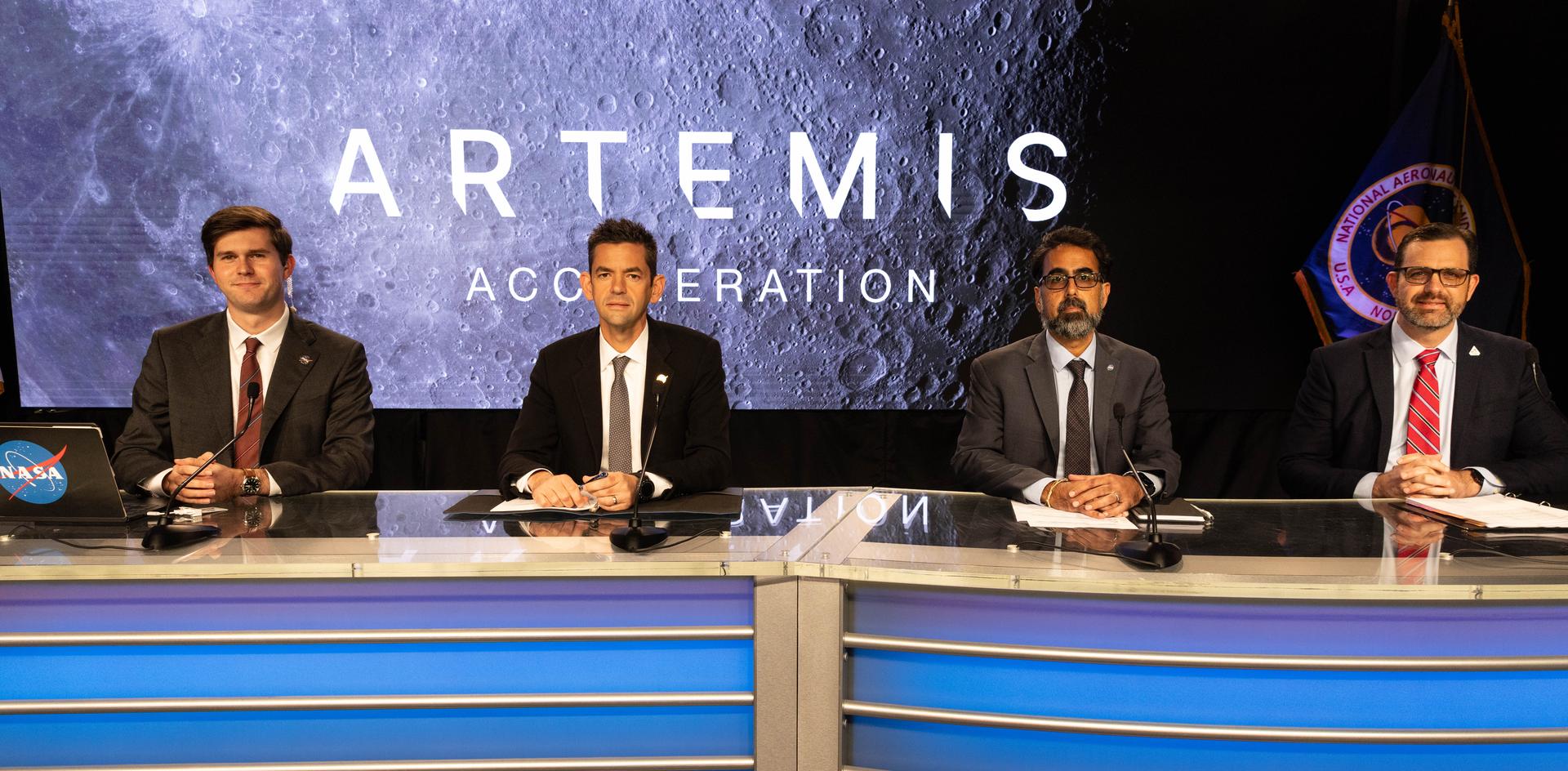 Four officials sit behind microphones at NASA’s Artemis Acceleration briefing, with a lunar backdrop.