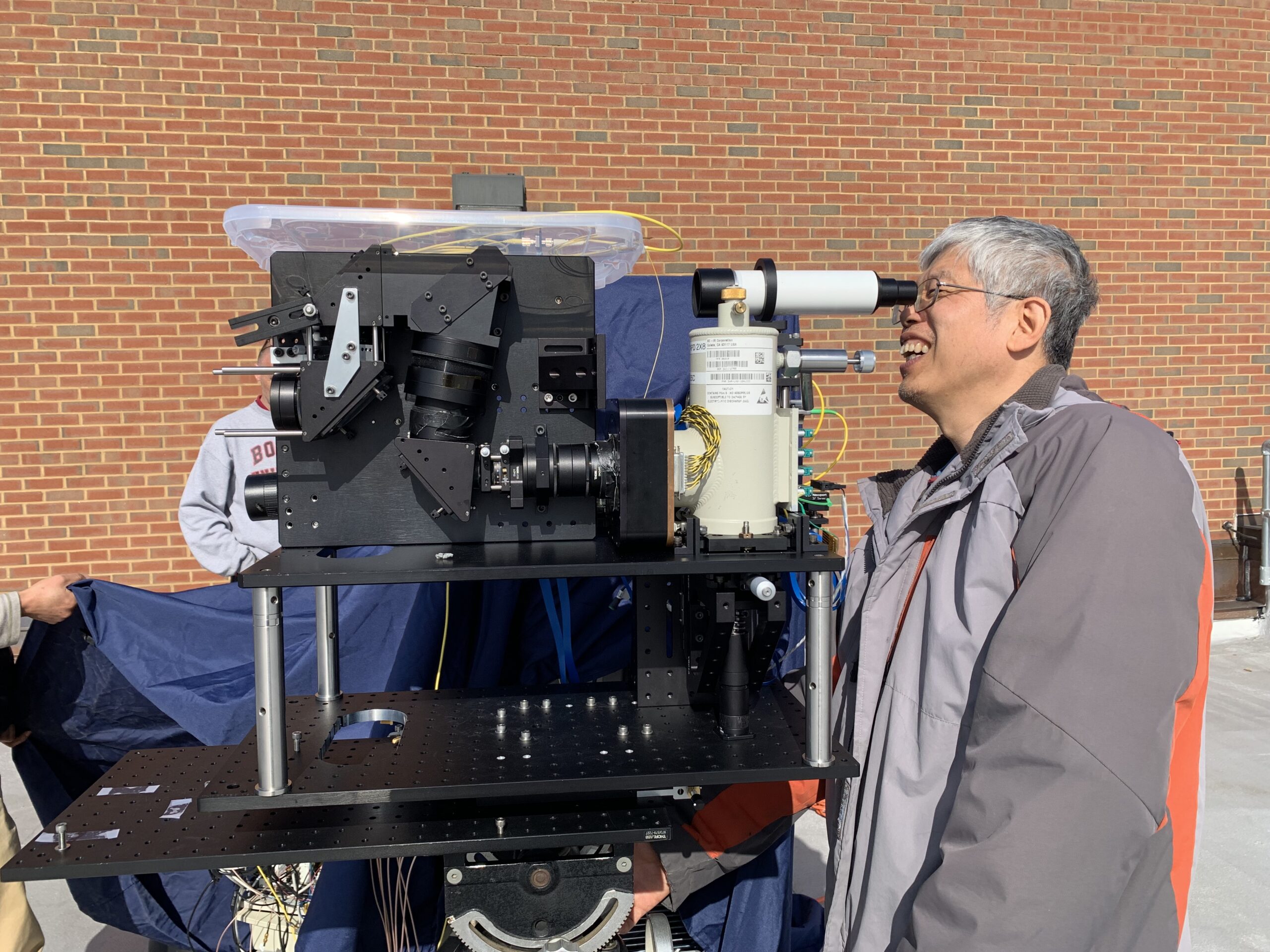 Engineer Jeffrey Chen looks through an eyepiece beside a lidar prototype on a rooftop at NASA Goddard.