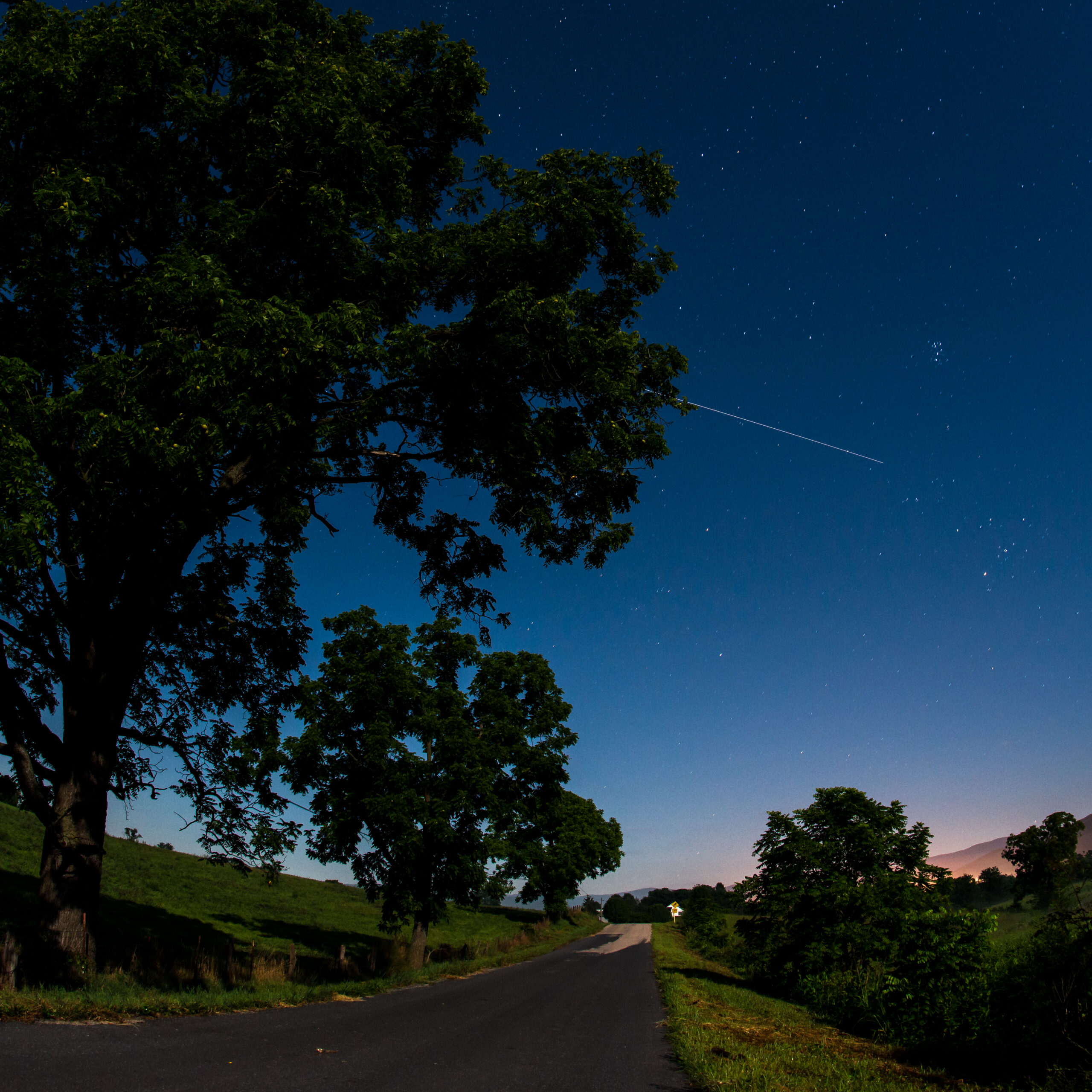 A long-exposure trail from the International Space Station crosses a starry sky above a rural road.