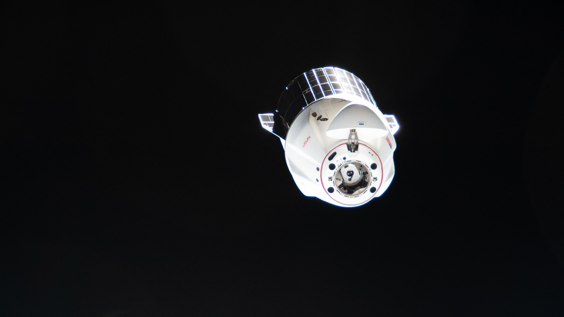 A SpaceX Dragon cargo spacecraft moves away from the International Space Station against black space.
