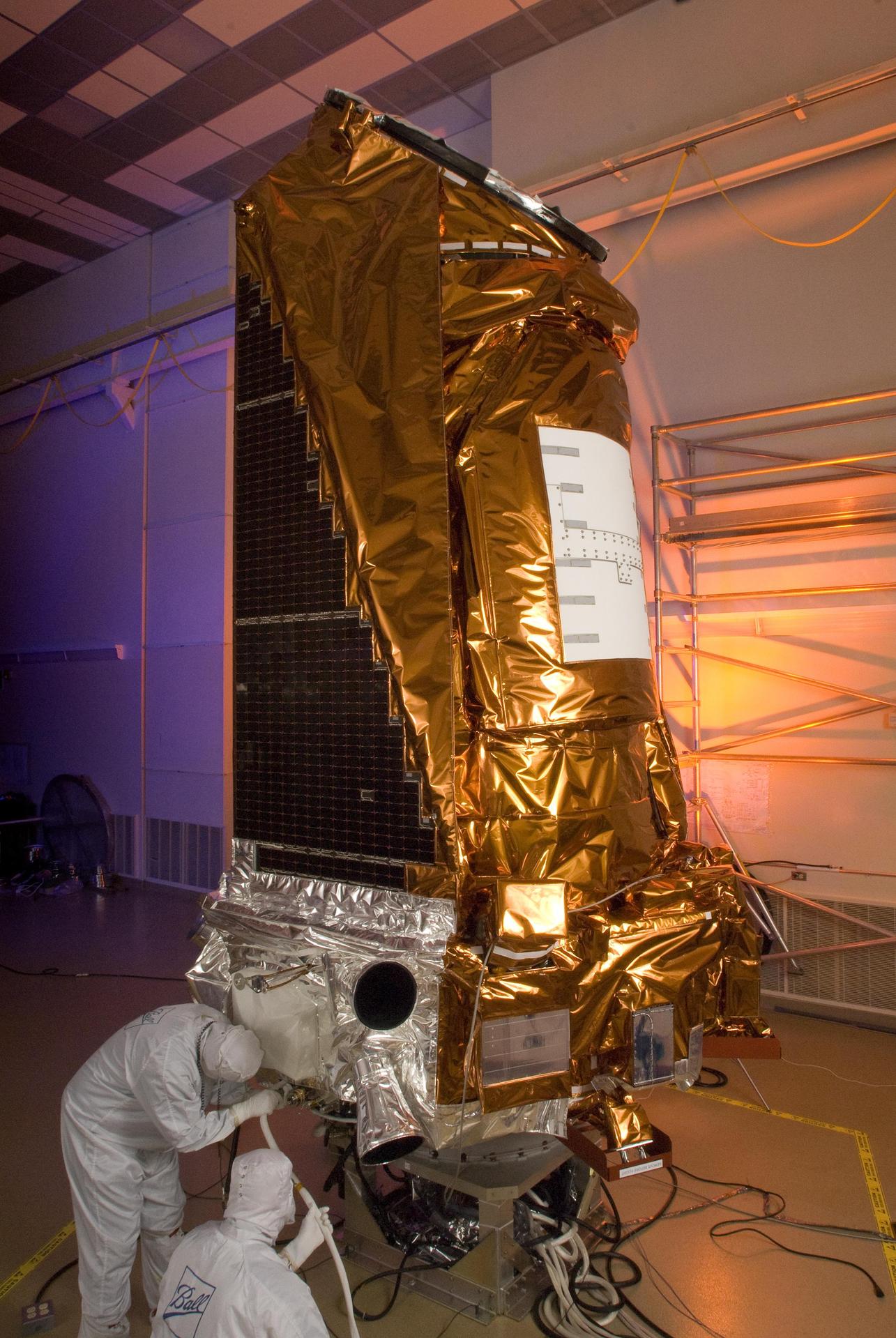 NASA’s gold-wrapped Kepler spacecraft during prelaunch preparation, with technicians working at its base.
